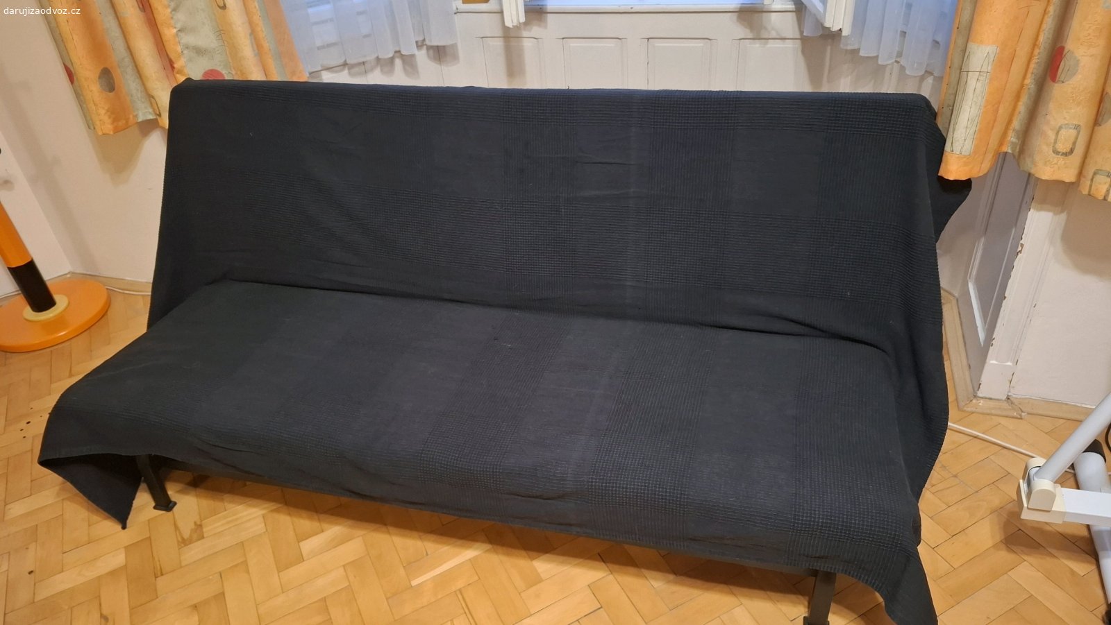 Rozkládací gauč. Na železné konstrukci je lamelový rošt a na něm dvoudílná molitanová matrace a černý přehoz. Rozměry 180x60cm, rozložený 180x120cm